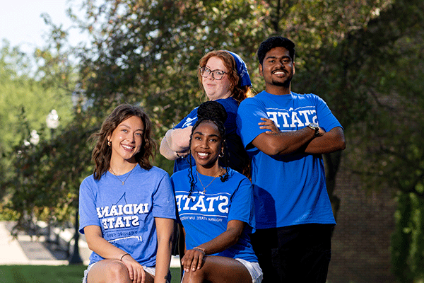 Four students – three female and one male – pose for a group photo, with each one wearing a blue Indiana State University shirt outside in the summer.